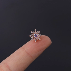 Macro view of a tiny rose gold flower stud earring with iris zircon on a fingertip