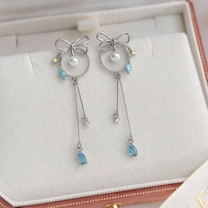 Detail of silver bow earrings with blue teardrop gemstone and pearl in a white gift box