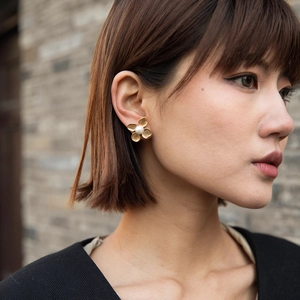 Detail of flower earrings with gold petals and white pearl worn by a model