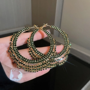 Dettaglio delle nappe di strass color smeraldo su orecchini a cerchio placcati in oro