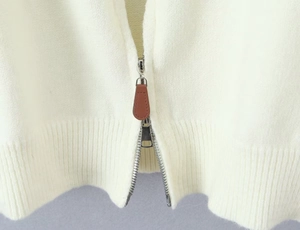 Detailed macro view of high-quality silver metal zipper with brown leather puller on cardigan