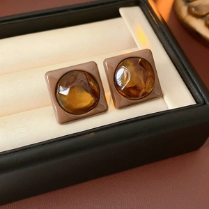 Close-up of square amber earrings with faceted gems set on a beige cushion in a black box