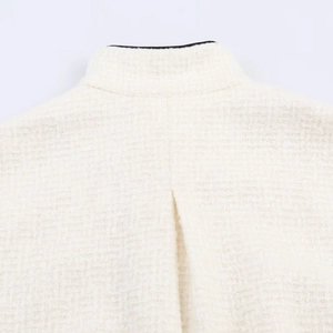 Detailansicht der gewebten Tweed-Struktur und Nähte einer beigen Stehkragenjacke