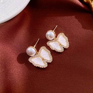 Macro view of gold plated butterfly pearl earrings with zircon inlay on silk background