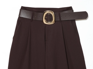 Detail of high-waisted dark brown trousers with a belt and polished gold metal buckle