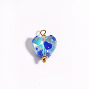 Macro detail of a heart-shaped blue glass charm with a gold metal pin for DIY jewelry