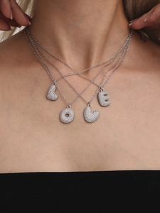 Close-up of four silver zircon letter pendants spelling LOVE on delicate necklaces
