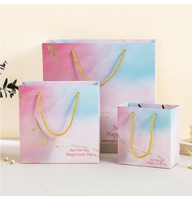 Three sizes of gradient pink and blue paper gift bags with golden rope handles and stars