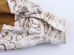 Detail of elegant lace embroidery on brown sleeve cuff with a white button closure