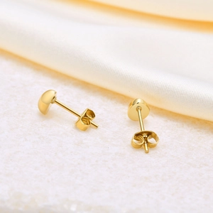 Detailed close-up of golden bean stud earrings on white marble and silk background