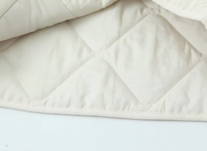 Close-up of cream quilted fabric with diamond stitching and neat edge piping on jacket