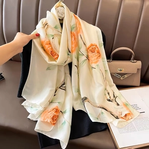 Elegant beige satin scarf with orange floral pattern and green leaves on black hanger