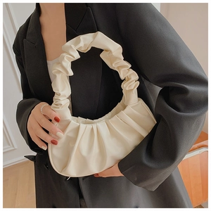 Close-up of beige pleated cloud bag with soft handle worn over a black blazer