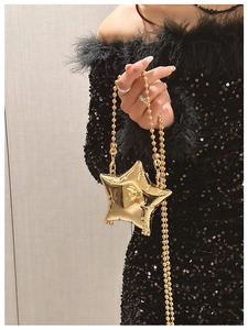 Detail of a golden star shaped mini bag with mirror finish and elegant metallic bead chain