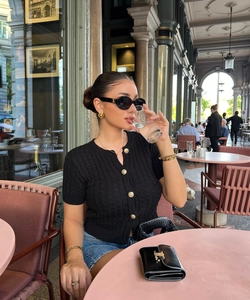 Detail of a black knit cardigan with gold buttons and vintage sunglasses in an outdoor cafe