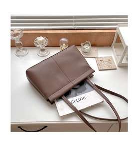 Deep brown minimalist faux leather tote bag with slender straps on a desk setup