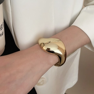 Dettaglio di bracciale rigido dorato spesso con linee irregolari e finitura a specchio lucida