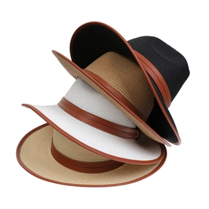 Detail view of stacked straw sun hats in black and beige with brown leather bands