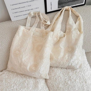 Close-up of white floral lace embroidery and hollow patterns on large canvas tote bags
