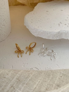 Detailed view of silver and gold bow-shaped hoop earrings on white stone props