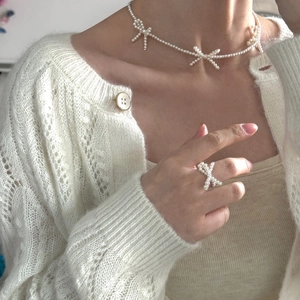 Elegant white pearl beaded bow necklace and ring set worn with a white knit cardigan