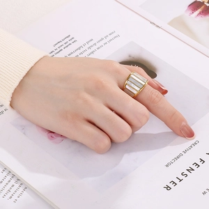 Detail of wide gold band ring featuring colorful shell inlay worn on a hand over a magazine