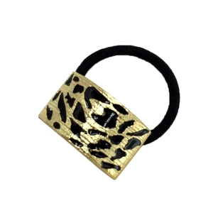 Detail of minimalist gold metal hair tie with black leopard enamel pattern