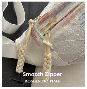 Detail of white textured chest bag with colorful embroidery and sturdy double zippers