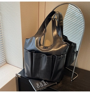 Detail of black leather tote bag with glossy finish and external utility pockets