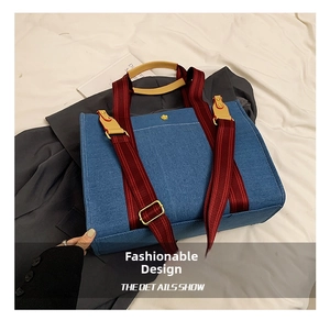 Detail of large denim tote bag with red striped handles and adjustable shoulder strap
