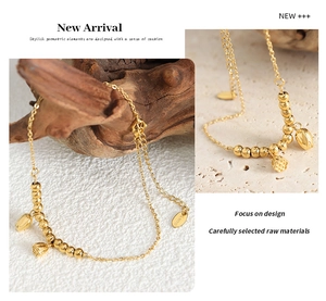 Detail of a gold stainless steel lotus charm bracelet on dark wood and stone base