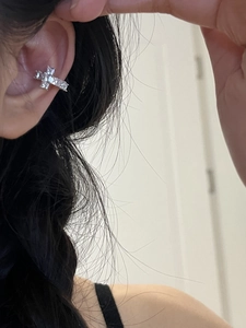 Close-up of a silver cross ear cuff with sparkling zircon stones worn on the ear