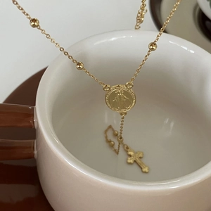 Detail of gold rosary necklace with Virgin Mary medal and cross pendant on a white cup