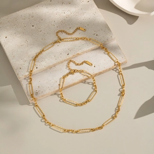 Golden stainless steel geometric chain necklace and bracelet set on stone background