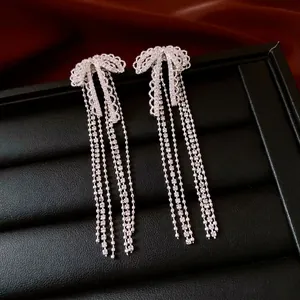 Elegant silver bow earrings with long zircon tassels on a black luxury jewelry box