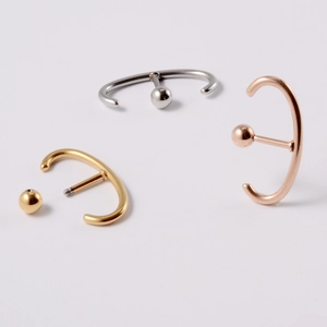 Three minimalist stainless steel C-shaped ear studs in gold, silver, and rose gold finishes