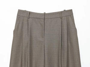 Detail of high-waisted taupe trousers showing double pleats and concealed button fly