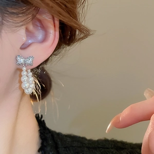 Close-up of bow earrings with sparkling zircons and hanging white pearl tassels on model