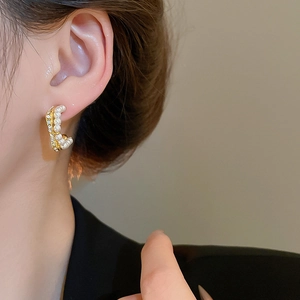 Close-up of golden C-shaped earrings with dual rows of pearls and sparkling crystals