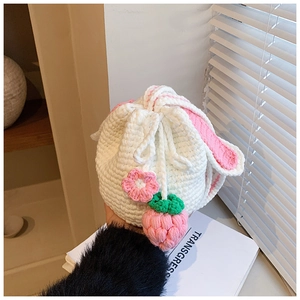 Detail of a handmade crochet strawberry bucket bag with pink rabbit ears and white knit texture