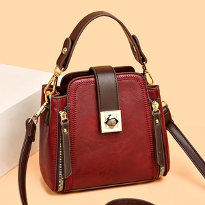 Fashionable burgundy bucket bag with brown straps and gold buckle on a stone stand