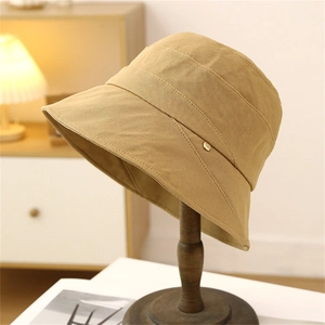 Minimalist khaki cotton bucket hat with gold metal buckle detail on a wooden stand