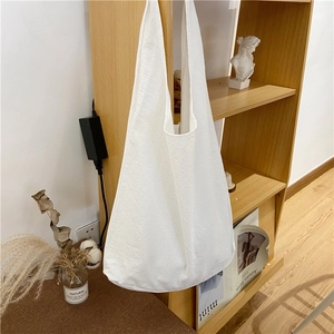 Minimalist white canvas tote bag with a natural cotton texture hanging on a wooden bookshelf