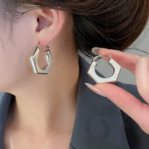 Detailed view of silver hexagonal metal hoop earrings worn to show polished finish