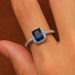 Close-up of silver ring with rectangular blue gemstone and pavé-set zircons on hand