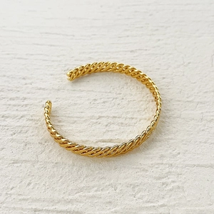 Macro detail of gold-plated twisted rope texture on an open cuff bracelet design