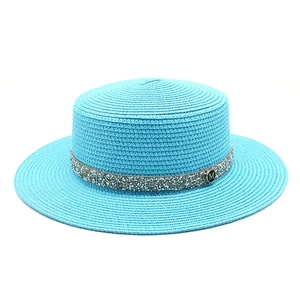 Close-up of bright blue straw boater hat with silver sequin band and metallic M logo