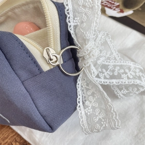 Detail of blue canvas makeup bag featuring cream lining and delicate white lace bow accent