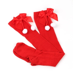 Close-up of red over-the-knee Christmas socks with satin bows and white fuzzy pom-poms