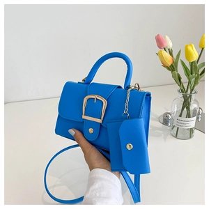 Detail view of a bright blue lychee grain leather crossbody bag with a large gold buckle